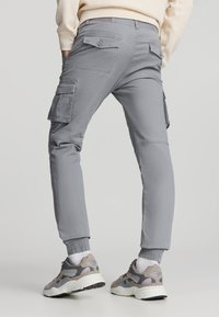 Pantaloni cargo grigi con tasche laterali, polsini elasticizzati e una trama liscia, abbinati a sneakers grigie e beige.