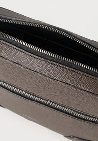 Κοντινό πλάνο γκρι δερμάτινης τσάντας με υφή, με δύο ανοιχτές ασημένιες φερμουάρ και μαύρη εσωτερική επένδυση σε λευκό φόντο.