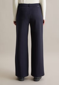 Marineblauwe wijde broek met een gladde textuur, voorzien van een getailleerde tailleband en discrete zakdetails, gecombineerd met zwarte plateauzolen.