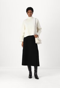 Maglione di maglia crema con maniche a 3/4, collo alto e orlo a coste; abbinato a una gonna nera maxi e stivali neri lucidi fino al ginocchio. Borsa bianca.