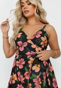 Vestido negro con estampado floral que presenta vibrantes flores en tonos rosa y naranja, diseño cruzado, tirantes finos y una alta abertura que revela una parte inferior a juego.