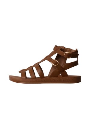 Sandale plate en cuir marron avec plusieurs brides et deux boucles dorées, vue de profil sur fond blanc.