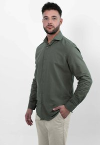 Groene lange mouw shirt met een kraaghalslijn, knopen aan de voorkant en een gladde textuur, gecombineerd met lichte broek.