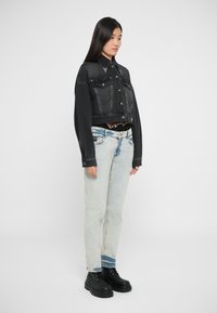 Črna skrajšana denim jakna z dvema sprednjima žepoma, v kombinaciji s svetlim naravnim ravnimi kavbojkami in črnimi vezalnimi čevlji.