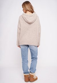 Beżowa dzianinowa bluza z kapturem o luźnym kroju i ściągaczu u dołu, zestawiona z jasnoniebieskimi dżinsami i brązowymi botkami z kontrastowym kożuchem.
