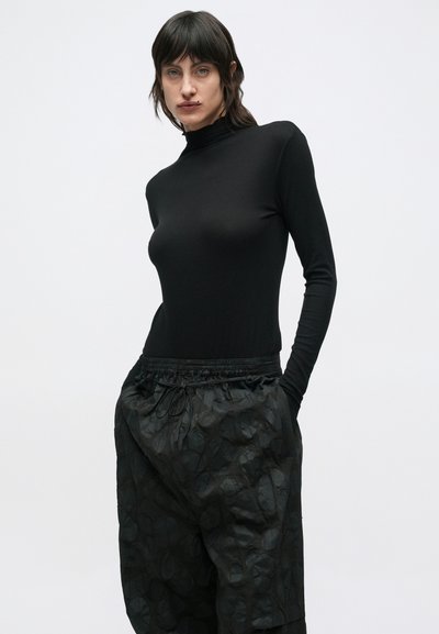 Μαύρο μπλουζάκι με μακριά μανίκια, στενή εφαρμογή και ψηλό λαιμό. Συνδυάζεται με φαρδιά, υφασμάτινα μαύρα παντελόνια με ελαστική μέση.