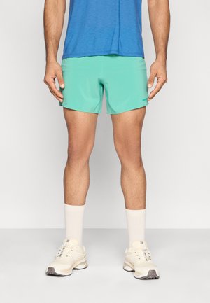 Turkusowe spodenki kąpielowe o gładkiej fakturze z elastycznym paskiem w talii, połączone z niebieską koszulą i białymi sportowymi butami z jasnymi akcentami.