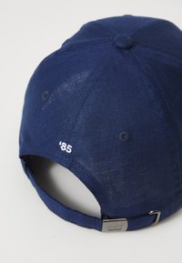 Cappello blu navy realizzato in tessuto leggero, dotato di un '85 ricamato in bianco sul retro e una chiusura con fibbia metallica regolabile.
