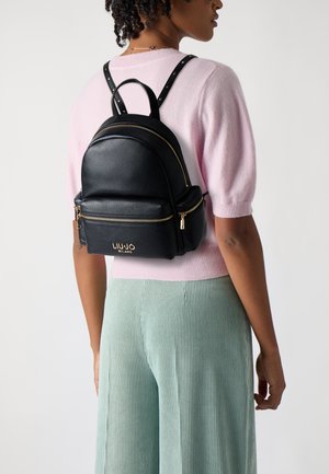 Schwarzer Leder-Rucksack mit zwei Reißverschlusstaschen, goldenen Hardware-Details und genieten Riemen. Rundes Design, kompakte Form.