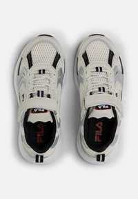 Baskets de sport en mesh blanc avec un design gris et noir, dotées d'une fermeture à sangle et d'une semelle rembourrée. Logo Fila sur la languette.