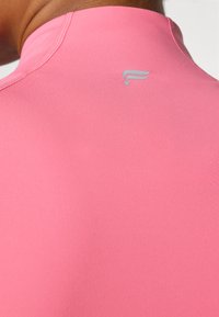 Fitted athletic top in bright pink, featuring a smooth texture and a high neckline. A small logo is visible on the back.
