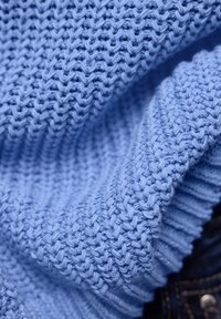 Gros plan sur un tissu tricoté bleu clair avec un motif de point texturé, montrant des plis et les détails de fil doux et épais.