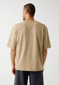 Beige cotton t-shirt with short sleeves, relaxed fit. Features a round neckline and a smooth, plain texture. Back view shows no graphics or accents.