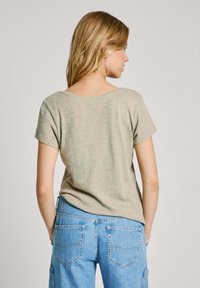 Camiseta corta de manga corta en verde claro con escote trasero en forma de barco, combinada con jeans azules con bolsillos traseros y un corte relajado.