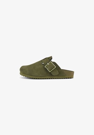 Sabots en daim vert olive avec une semelle plate, boucle latérale réglable et semelle extérieure texturée en zigzag. Design à bout fermé avec un profil minimaliste.