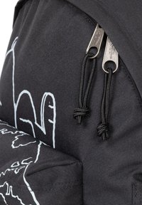 Mochila negra con tejido suave, cremalleras metálicas dobles y un diseño gráfico en blanco. Incluye cordones negros anudados para el cierre.