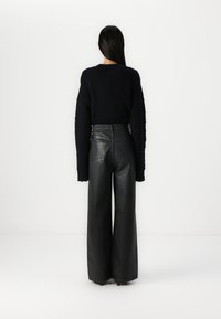 Black knitted sweater with long sleeves and a textured design, paired with high-waisted black leather wide-leg pants featuring back pockets.
