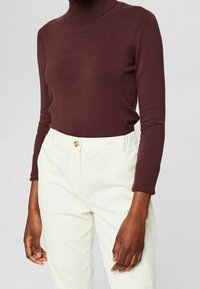 Maglione a dolcevita color bordeaux con dettagli a coste abbinato a pantaloni in velluto a coste crema con chiusura a bottone e vita elasticizzata.