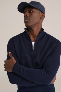 Tumši zils džemperis ar ceturtdaļas rāvējslēdzēju un teksturētu dziju, papildināts ar atbilstošu cepuri. Dizainā ir garas piedurknes un brīvs piegriezums.