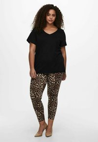 Crna majica s v-neck izrezom i kratkim rukavima, uparena s bež tajicama s smeškim leopard uzorkom. Model nosi bež štikle.