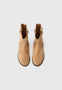 Stivaletti alla caviglia in suede tan con cuciture decorative bianche, cerniera laterale e dettagli cut-out sulla parte superiore. Suola piatta e texturizzata nera.