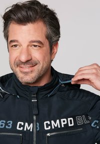 Black, hooded jacket with ribbed texture, front zip closure, and blue accents. Features printed logos and zippered pockets.