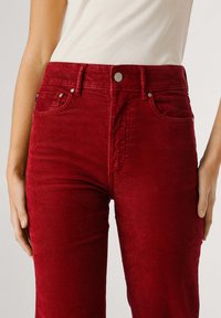 Pantaloni a vita alta in corduroy rosso con superficie rigata testurizzata, tasche frontali e dettagli in metallo in vita.