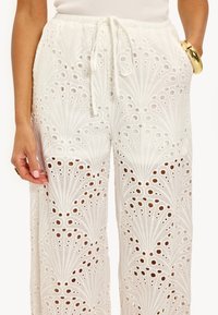 Witte, lichte broek met ingewikkelde uitsnijdingen en een drawstring taille. Geverfd stof met een losse, vloeiende snit.