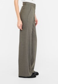 Pantaloni grigi chiari a vita alta con design a gamba larga, tessuto testurizzato, tasche laterali e passanti per cintura, abbinati a scarpe nere.