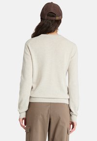 Maglione color crema con orlo e polsini a coste, realizzato in materiale morbido. Indossato con pantaloni cargo marroni e un berretto in velluto a coste marrone.