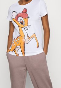 Vit bomulls T-shirt med en färgglad, tecknad hjortgrafik. Rund halsringning, korta ärmar, avslappnad passform och minimal textur.