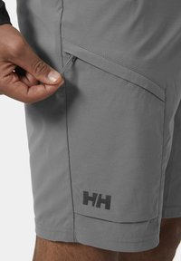 Šedé kraťasy vyrobené z lehkého materiálu, s boční kapsou na zip, plochým pasem a vyšitým logem na lemu.