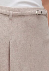 Helle beige Hose aus strukturiertem Stoff, mit flachem Frontdesign, Gürtelschlaufen und einem silbernen quadratischen Schnallenakzent am Bund.