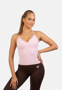 Jasnoróżowy top sportowy z dekoltem w serek i strukturalnym materiałem, zestawiony z ciemnobrązowymi legginsami z białym logo.