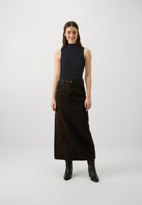 Schwarzes ärmelloses Top kombiniert mit einem langen, schokoladenbraunen Jeansrock mit Frontknöpfen und Taschen, ergänzt durch schwarze, absatzhohe Knöchelstiefel.