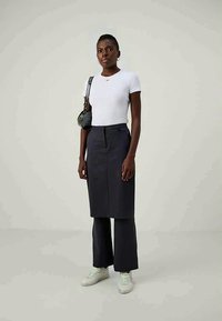 White short-sleeve t-shirt with a small red logo, paired with dark gray, high-waisted skirt-pants and white sneakers. Textured handbag.