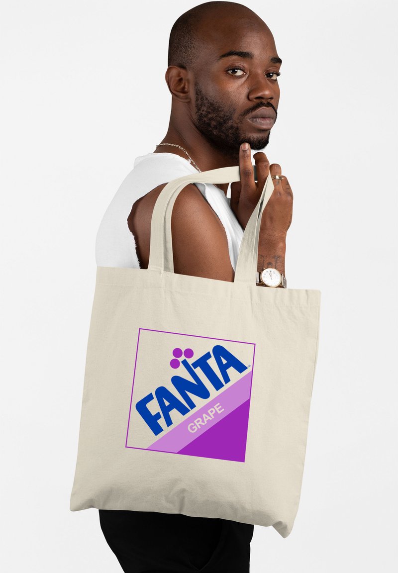 Beige canvas draagtas met een kleurrijk retro Fanta Grape-logo in blauw en paars, met een geometrisch ontwerp en stevige handvatten.