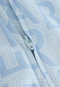 Svetlomodrá bunda na zips s geometrickým vzorom v o niečo tmavšom odtieni. Mäkkučký materiál s hladkým povrchom, praktický zips.