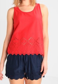 Röd ärmlös topp med scallop-hållare och ögonletsutsnitt samt blommönster; matchad med mörkblå shorts med scallop-hållare.