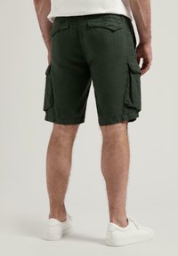 Grüne Cargo-Shorts mit Seitentaschen, lässiger Passform und einem weichen, strukturierten Stoff. Getragen mit weißen Sneakers vor einem neutralen Hintergrund.