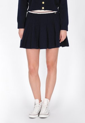 Gonna plissè blu navy con una trama in maglia e una cintura bianca a contrasto, abbinata a sneakers bianche alte.