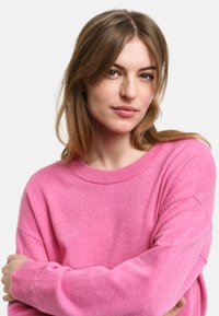 Rosa Kaschmirpullover mit rundem Ausschnitt, lockerer Passform und gerippten Bündchen. Weiche Textur und glatte Oberfläche ohne sichtbare Muster.
