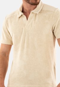 Polo shirt beige a maniche corte in morbido tessuto strutturato con colletto classico e un piccolo logo sul petto.