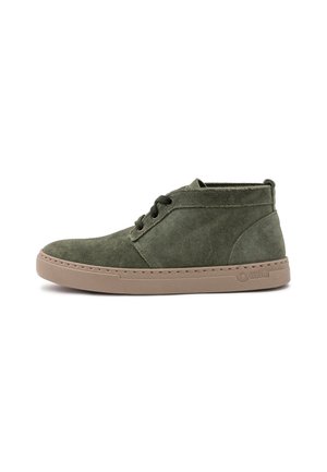 Botines de ante verde con suela de goma marrón, que cuentan con dos ojales y un detalle cosido alrededor de la suela. Textura suave y diseño minimalista.