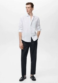 White linen button-up shirt, single chest pocket, worn with black tailored trousers and black loafers, set against a light background.