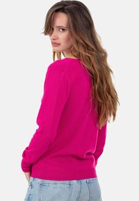 Fuchsienfarbener Pullover, leichter Strick, lange Ärmel, runder Ausschnitt, Rippbündchen, taillierter Schnitt, kombiniert mit hellblauen Jeans-Shorts.