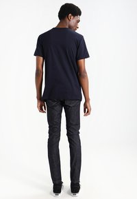 T-shirt a maniche corte blu navy abbinato a jeans in denim scuro. I jeans hanno una vestibilità slim e una texture sottile, mentre delle sneakers nere completano l'outfit.