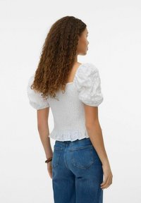 Top bianco con maniche a sbuffo, corpo arricciato e orlo volant, realizzato in tessuto testurizzato, abbinato a jeans in denim blu.
