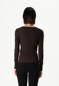 Braunes, geripptes Langarmoberteil mit rundem Ausschnitt, taillierter Form und glatter Textur, kombiniert mit schwarzen Jeans. Rückansicht.