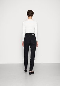 Schwarze hochgeschnittene Jeans mit geradem Bein, ausgestattet mit sichtbaren Gesäßtaschen und einem Markenetikett am Bund. Glatte Stofftextur.